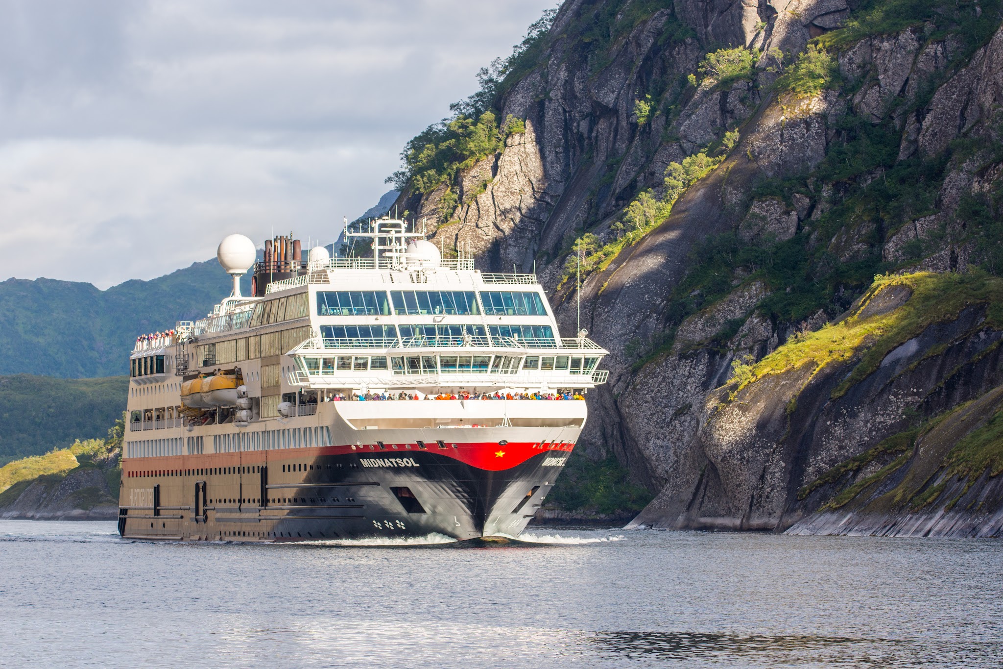 Kreuzfahrtschiff fährt durch engen, von steilen Felsklippen und Grün gesäumten Fjord.