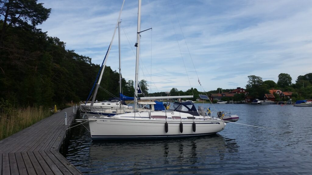 Segelboot am Holzsteg, ruhiger See mit Wald links und roten Uferhäusern im Hintergrund