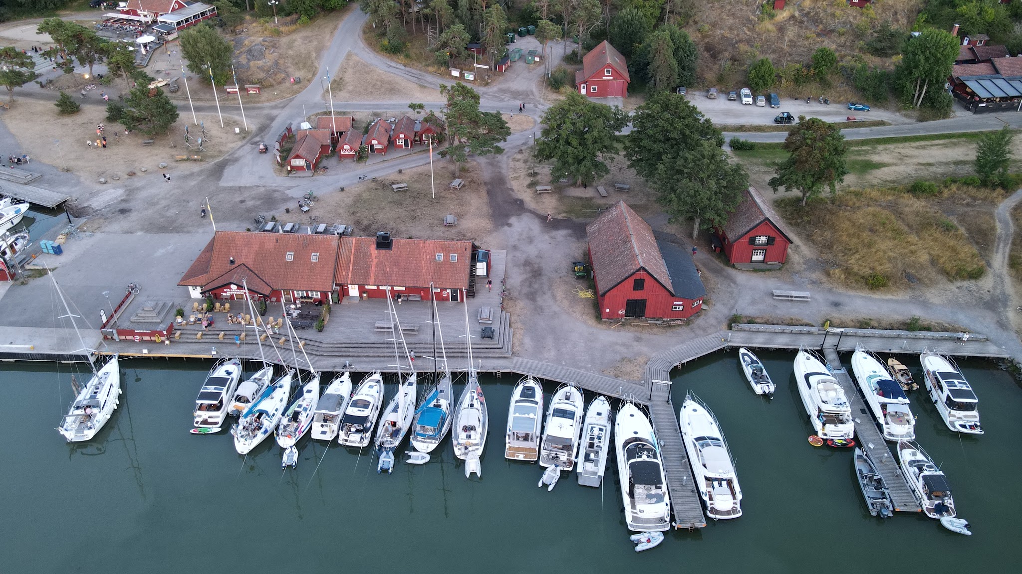 Marina aus der Luft: dicht aneinandergereihte Segel- und Motorboote vor roten Holzhäusern am Steg.
