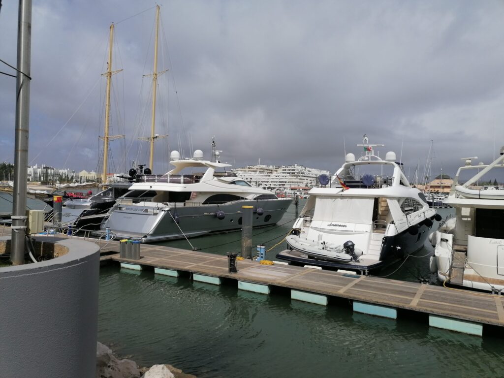 Mehrere Luxusjachten liegen an einem Holzsteg im Hafen unter grauem Himmel.