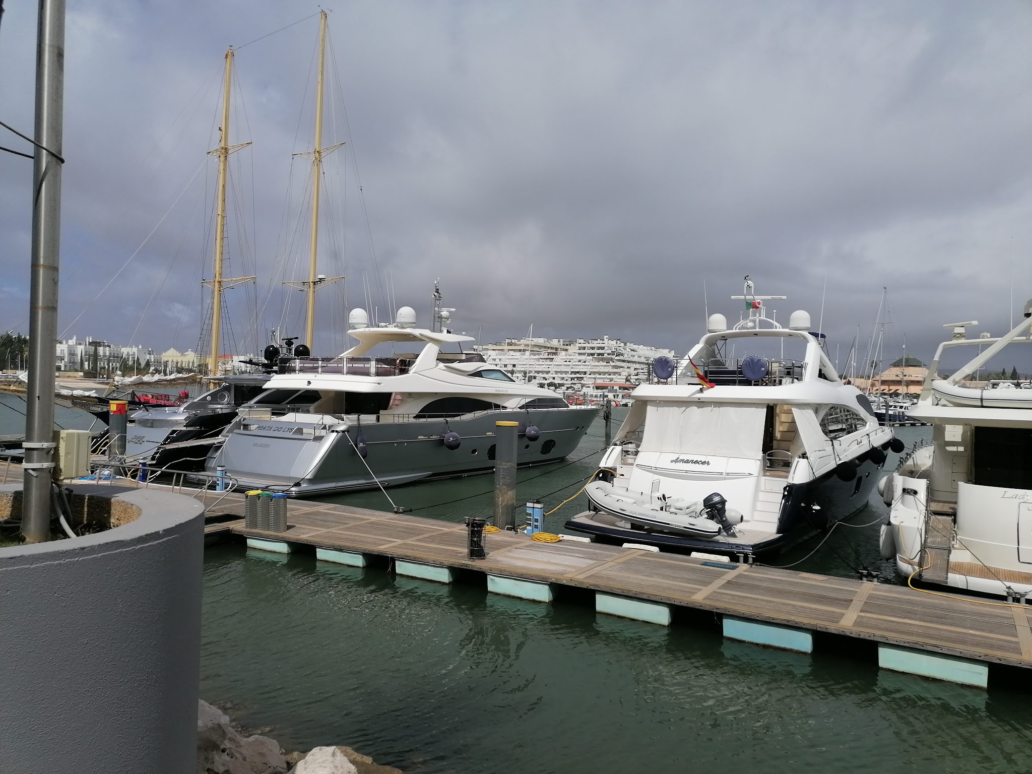 Mehrere Luxusjachten liegen an einem Holzsteg im Hafen unter grauem Himmel.