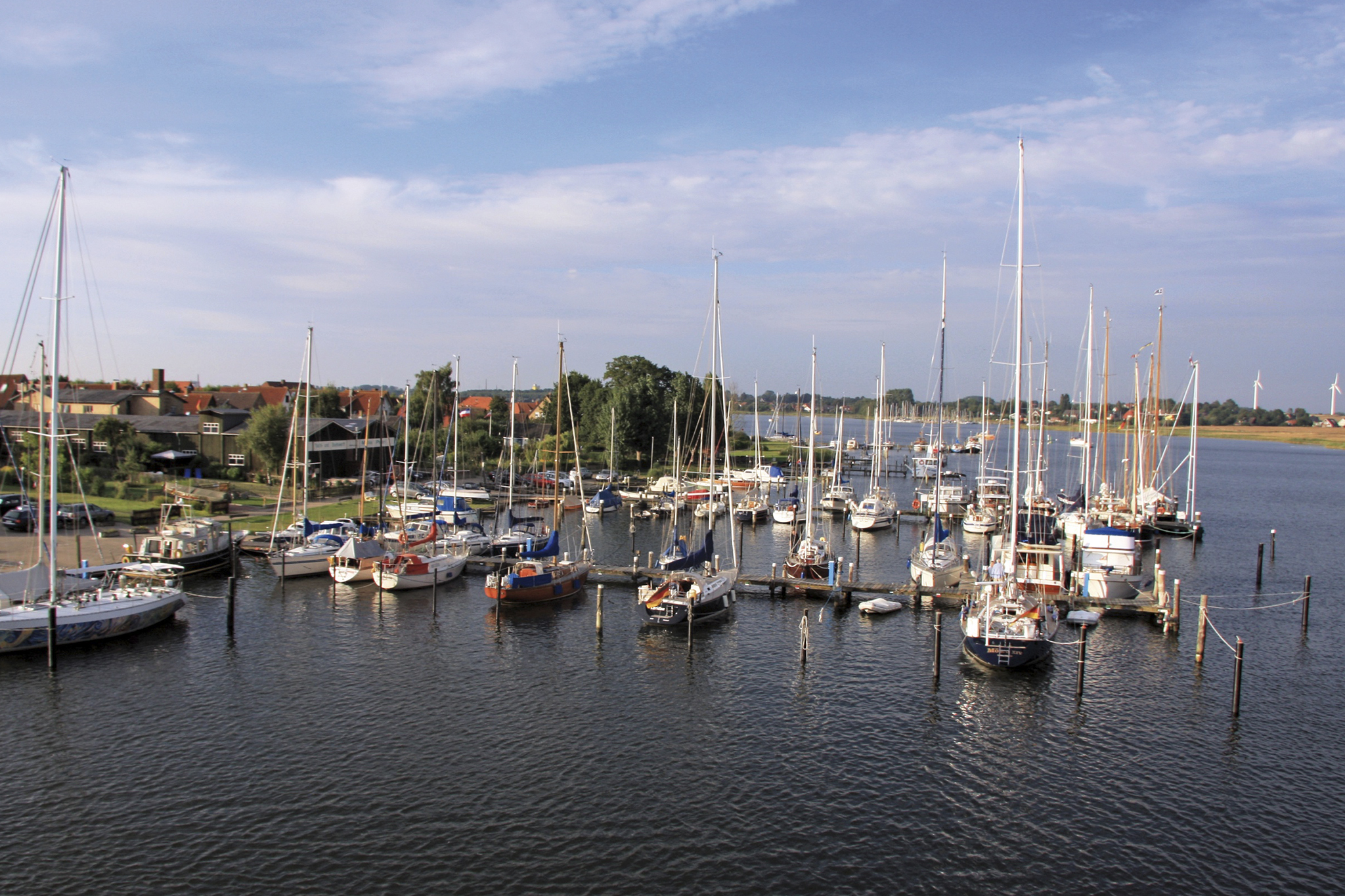 Kleiner Yachthafen: zahlreiche Segelboote liegen an Stegen vor Küstenort, ruhiges Wasser, blauer Himmel