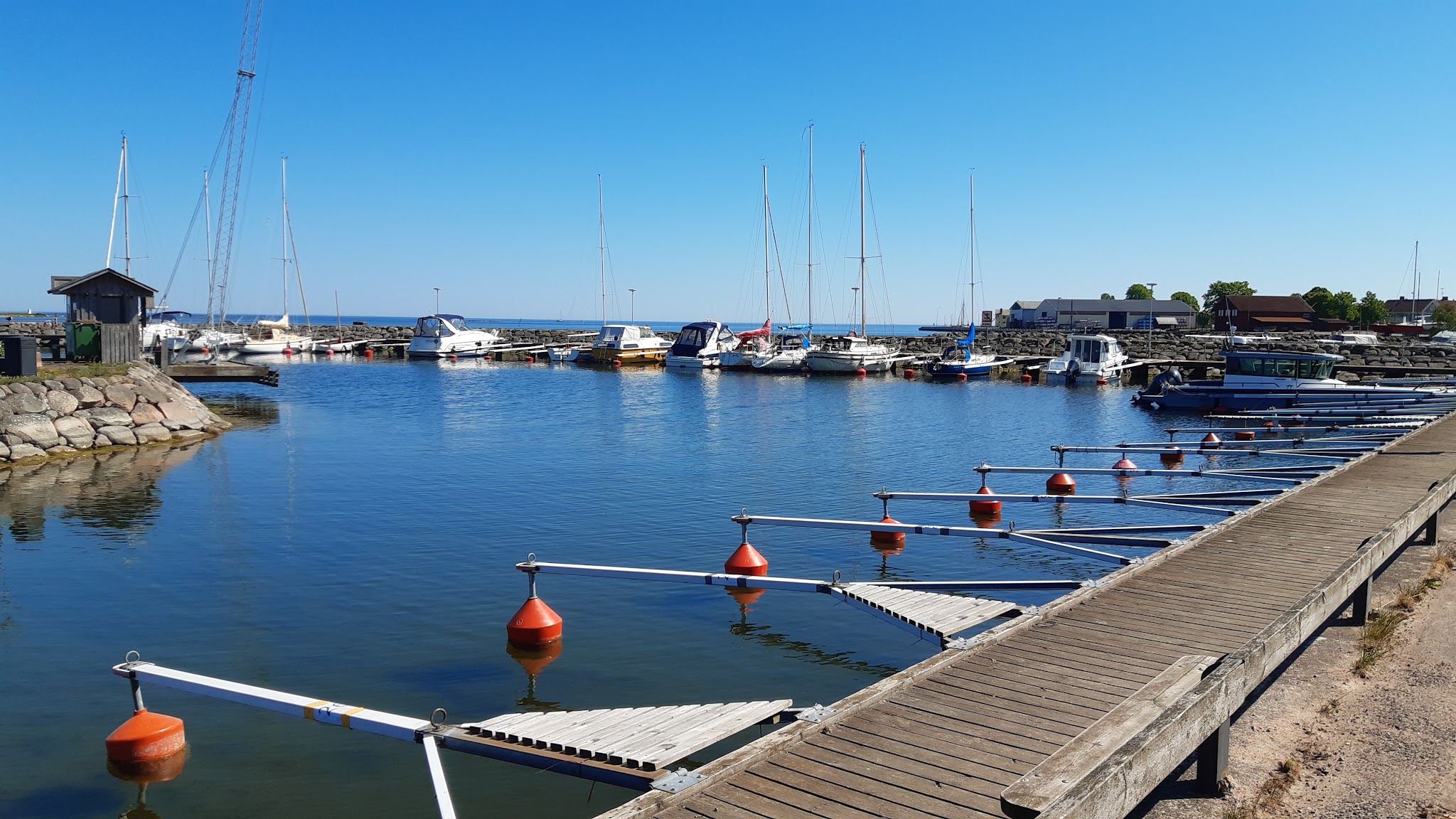 Ruhiger Yachthafen: anliegenden Segelboote, freie Holzstege und Bojen spiegeln sich im klaren Wasser unter blauem Himmel