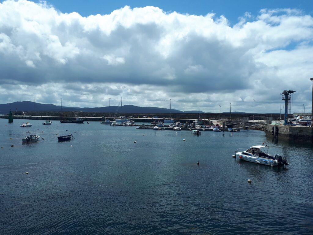 Kleiner Hafen mit mehreren ankernden Motor- und Segelbooten; stilles Wasser, bewölkter Himmel, Berge am Horizont