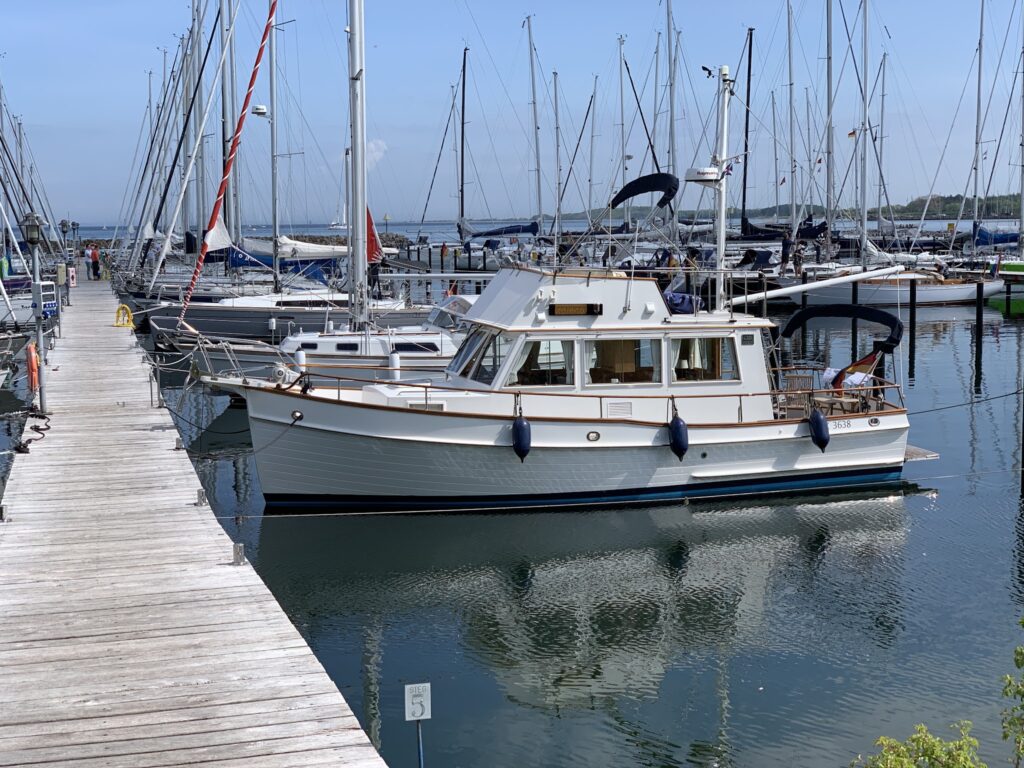 Weißes Motorboot am Holzsteg, umgeben von zahlreichen festgemachten Segelbooten im ruhigen Hafen.