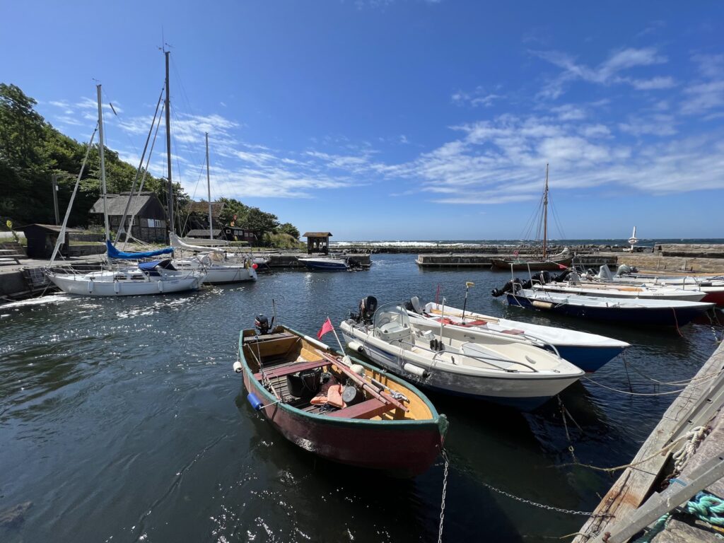Kleiner Hafen mit mehreren Segel- und Motorbooten, ruhiges Wasser, blauer Himmel mit leichten Wolken.