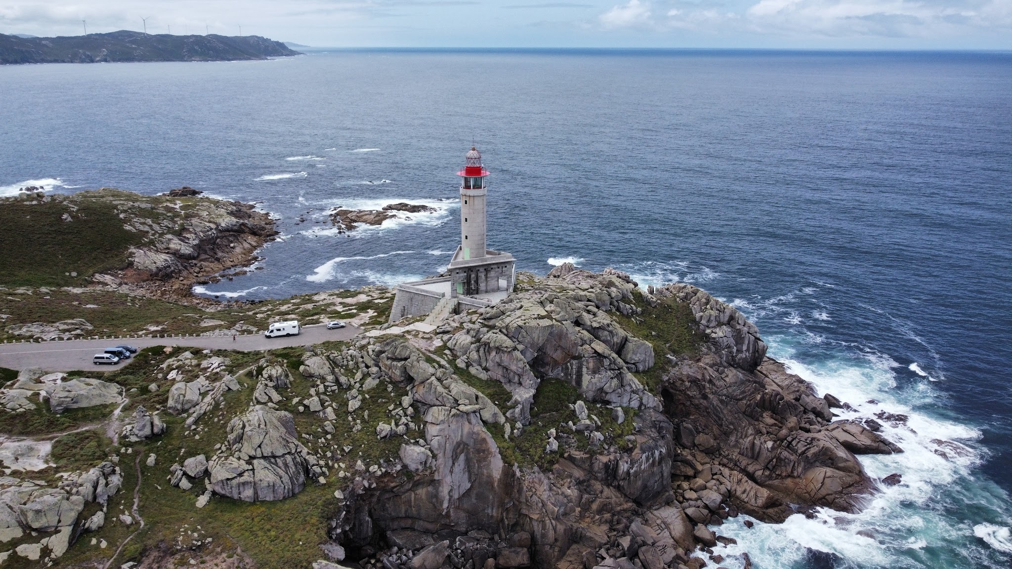 Leuchtturm mit roter Kuppel auf felsiger Klippe, umgeben von rauer Atlantikküste und schäumenden Wellen.