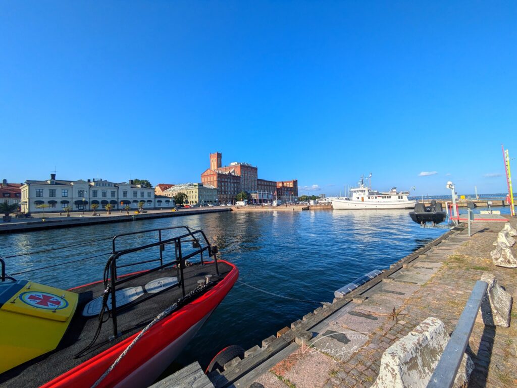 Sonniger Hafen; rotes Rettungsboot im Vordergrund, weiße Yacht dahinter, historische Speichergebäude am Kai.