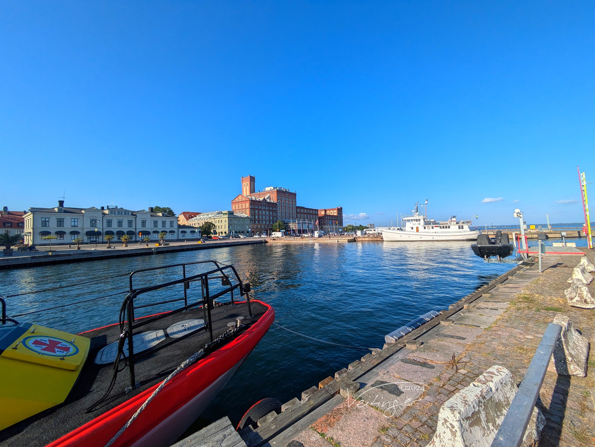 Sonniger Hafen; rotes Rettungsboot im Vordergrund, weiße Yacht dahinter, historische Speichergebäude am Kai.