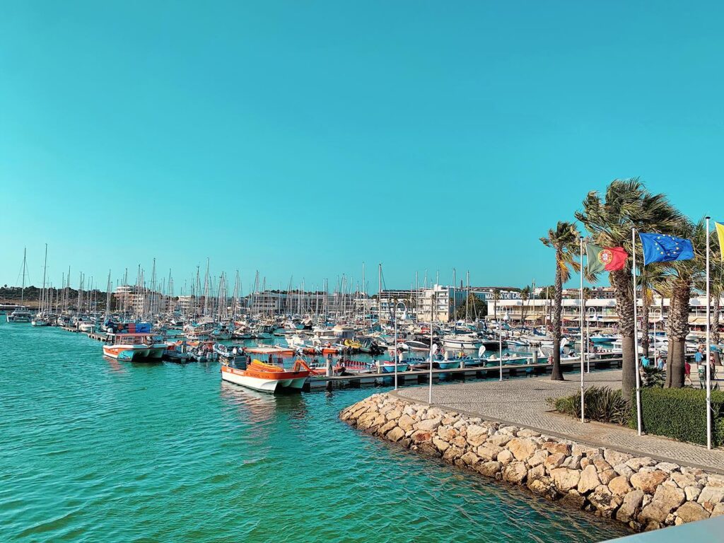 Sonniger Jachthafen: Dicht aneinandergereihte Segelboote, türkisfarbenes Wasser, Palmen und wehende Portugal- und EU-Flaggen
