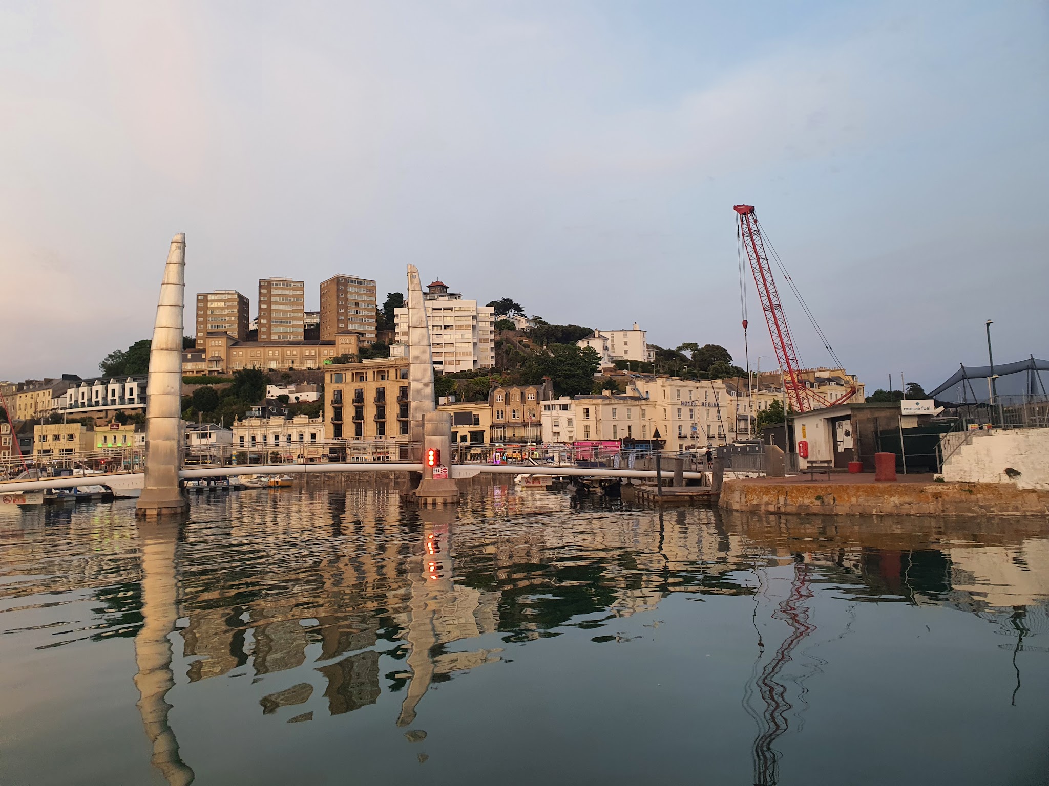 Hafenpromenade mit Klappbrücke, zwei geneigten Metalltürmen, Booten und Häusern, Spiegelungen im ruhigen Wasser