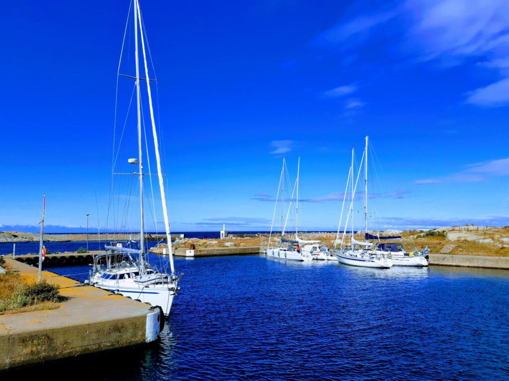 Mehrere Segelboote liegen bei sonnigem Wetter in einem kleinen Hafen mit klarem blauem Wasser.