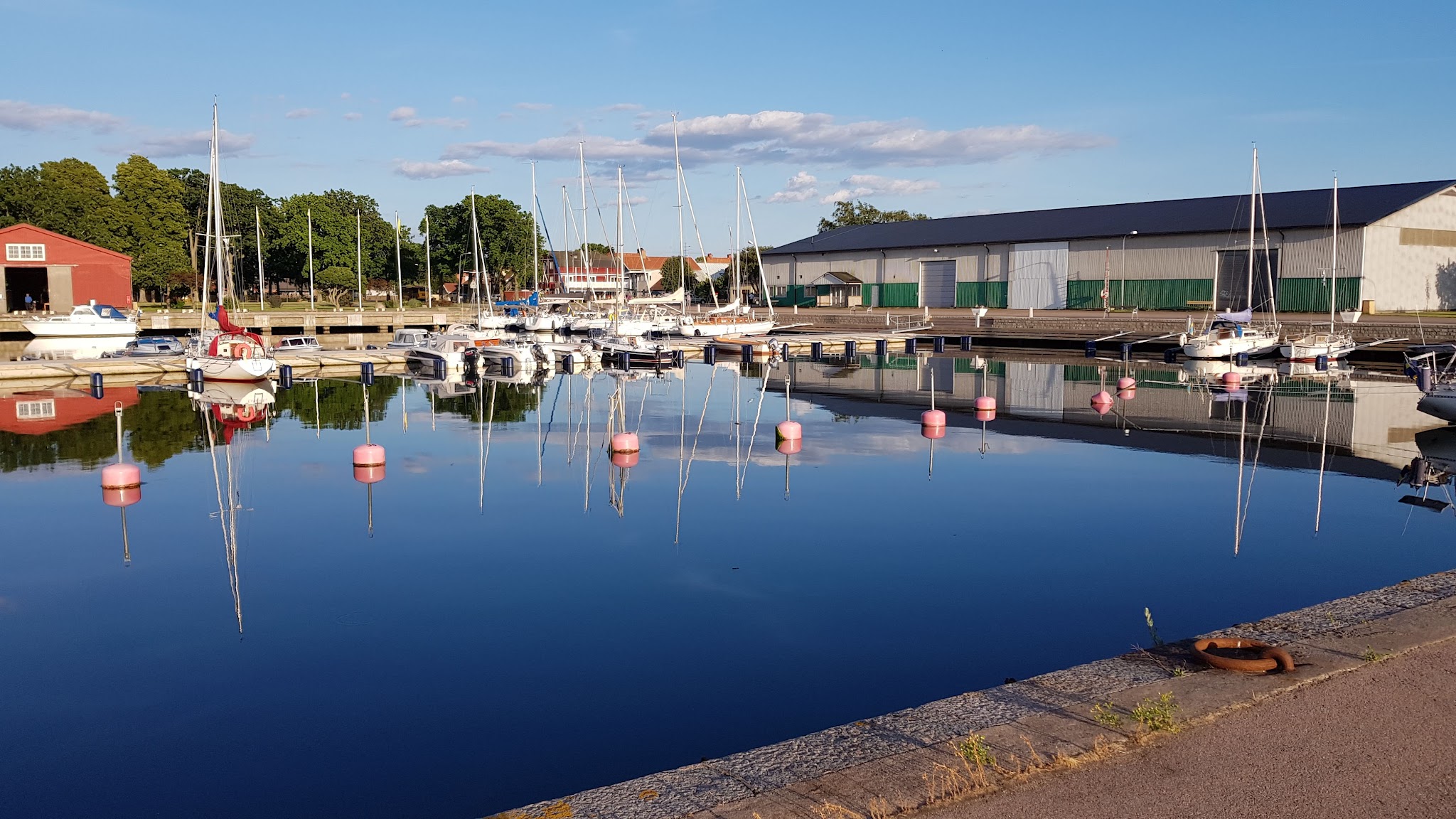 Ruhiger Hafen mit vertäuten Segelbooten, pinken Bojen und klarer Spiegelung von Booten und Himmel im stillen Wasser