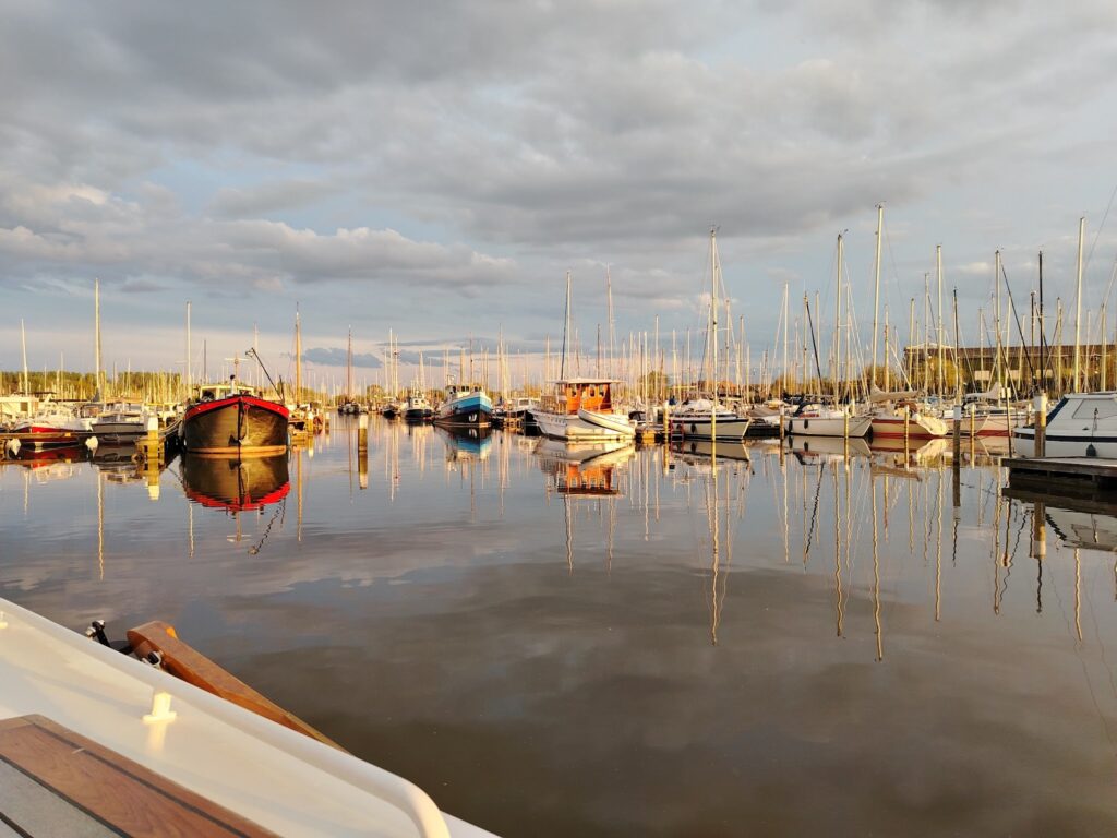 Ruhiger Yachthafen, dicht aneinander liegende Segelboote spiegeln sich im Abendlicht auf glatter Wasseroberfläche.