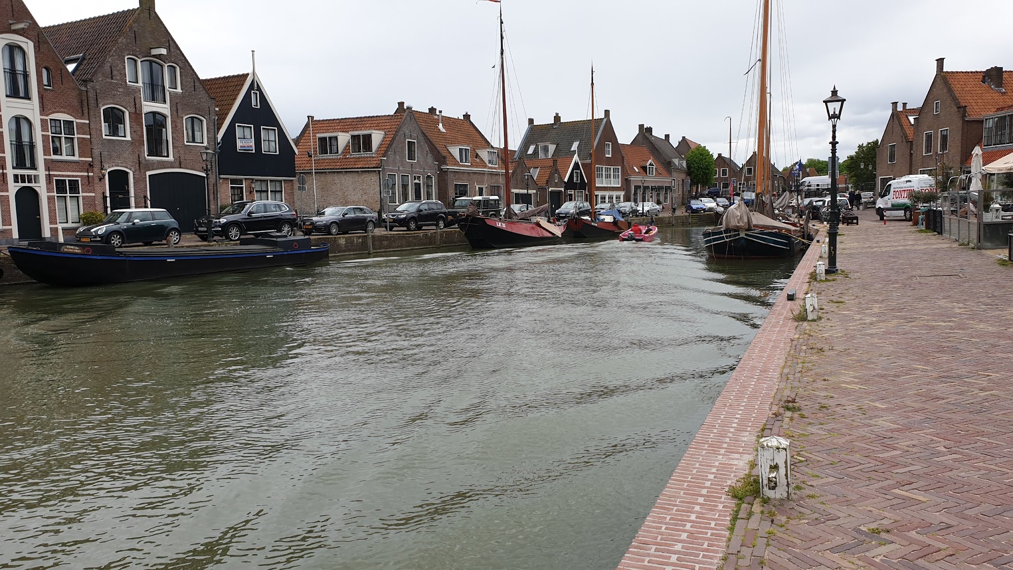 Kleiner Kanal mit historischen Segelbooten, Backsteinhäusern und Uferpromenade in einem niederländischen Städtchen.