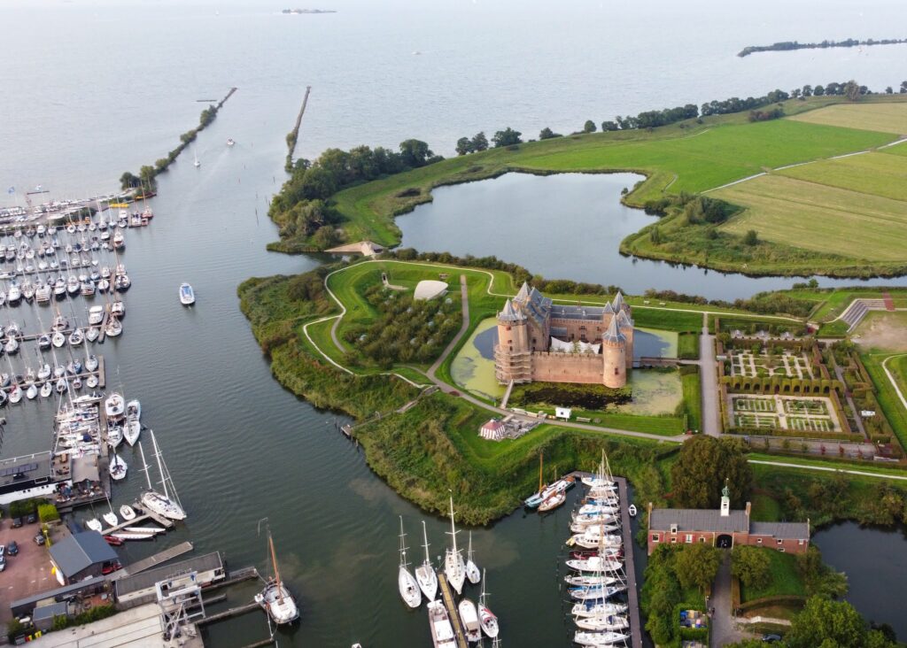Luftaufnahme einer Wasserburg auf Insel mit Gräben, umgeben von Yachthafen, Wasserwegen und grünen Wiesen.