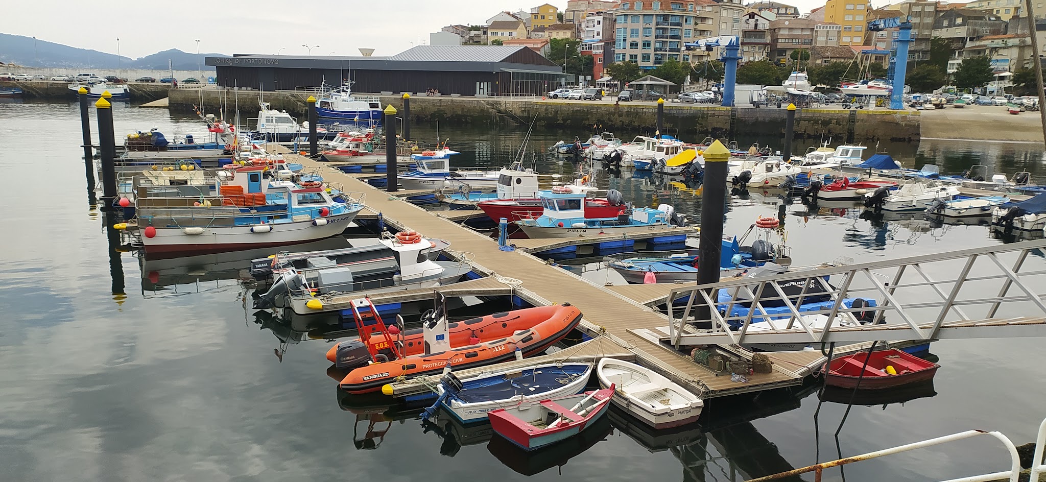 Zahlreiche kleine Fischer- und Motorboote liegen an schwimmenden Stegen in einem ruhigen Stadthafen.