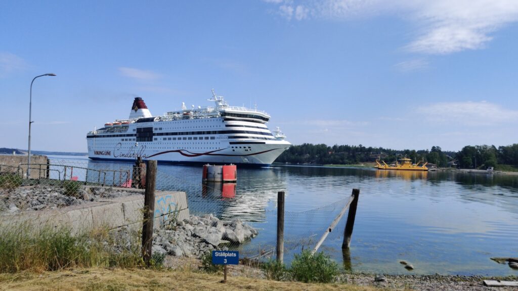 Große weiße Fähre Viking Line Cinderella fährt ruhig übers Wasser; hinten kleinere gelbe Fähre und Waldküste.