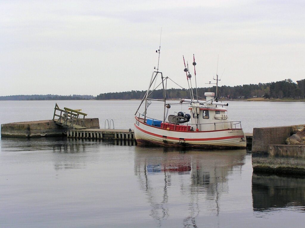 Kleines Fischerboot an verfallener Mole auf ruhigem Wasser unter bedecktem Himmel
