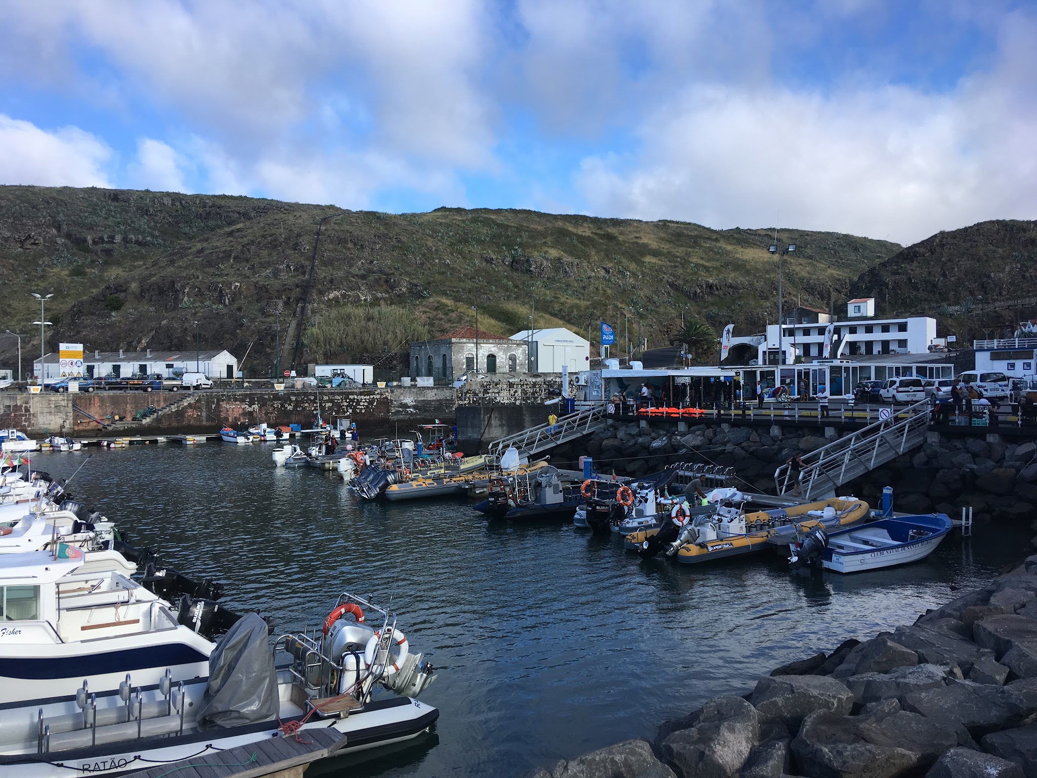 Kleine Boote im Hafenbecken vor steilen, grünen Felshügeln und weißen Hafengebäuden.